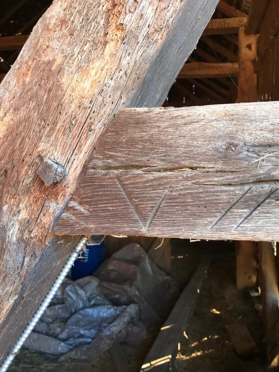 Close-up of weathered wooden beams joined with a triangular marking and a metal peg in a building's structure.