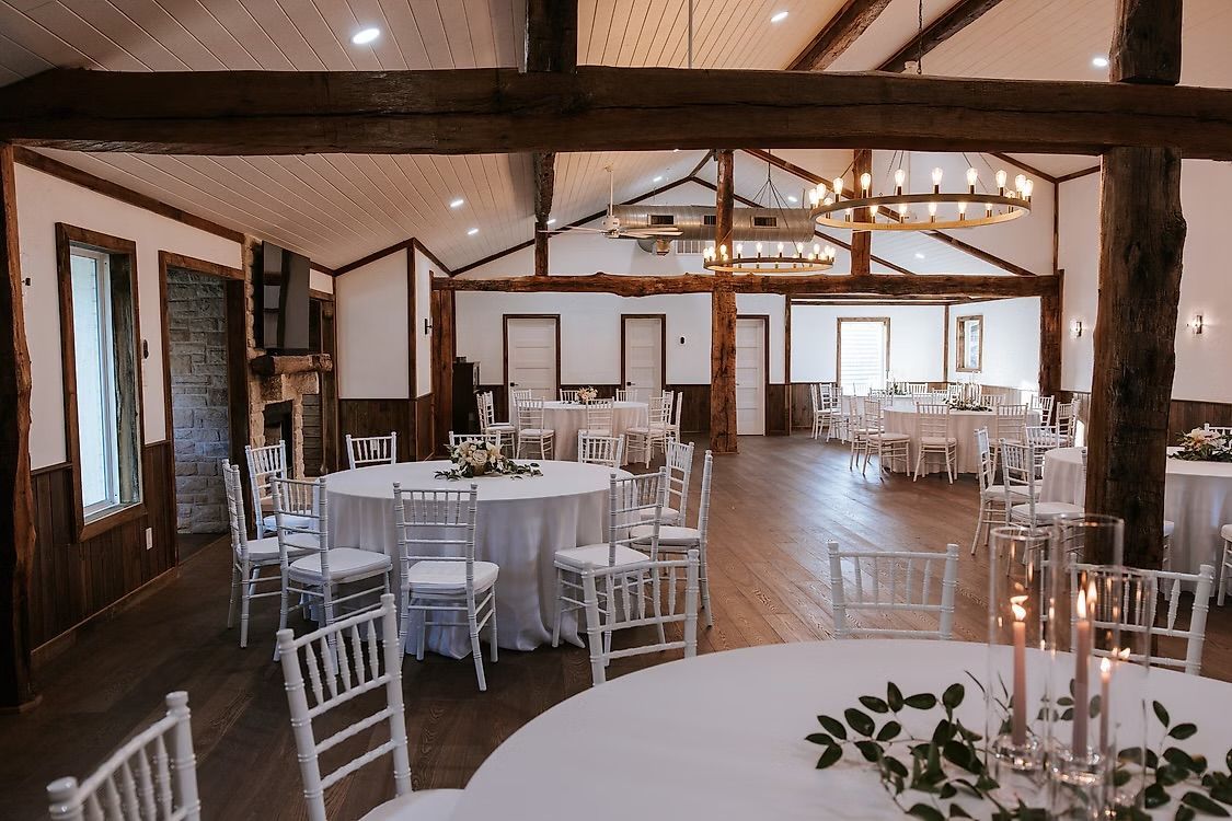 Ivey Cabin wedding reception hall with round tables set for guests. White linens and chairs, wood beams and a chandelier.