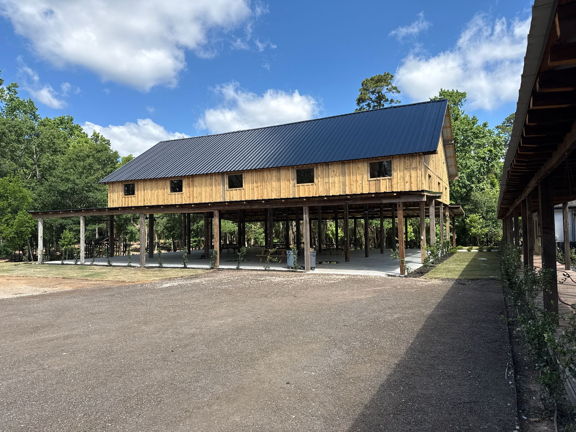 Wooden barn on stilts with dark blue roof, under a blue sky, surrounded by trees.