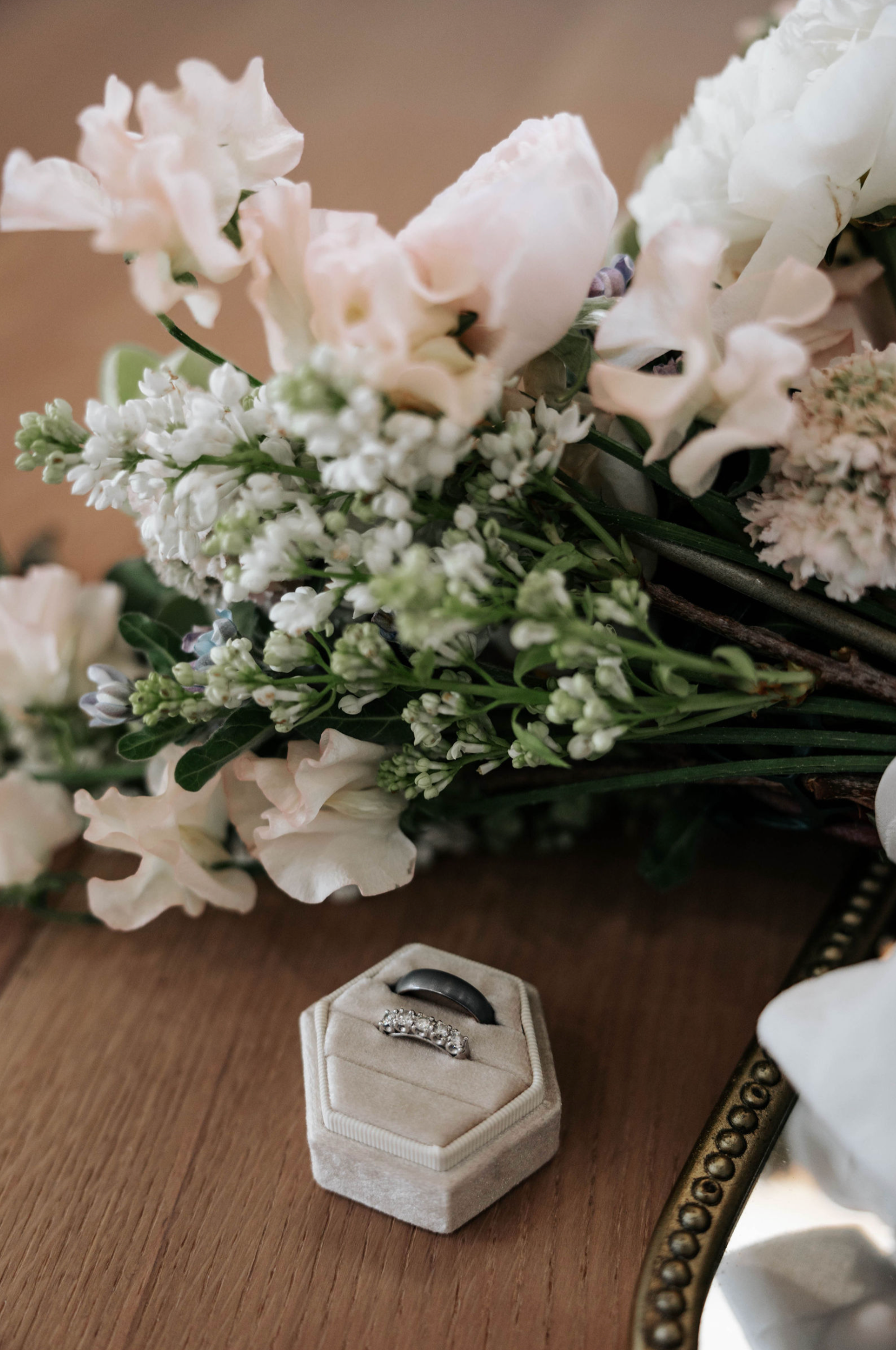 Wedding rings in a velvet ring box with a bouquet of white flowers on a wooden surface.