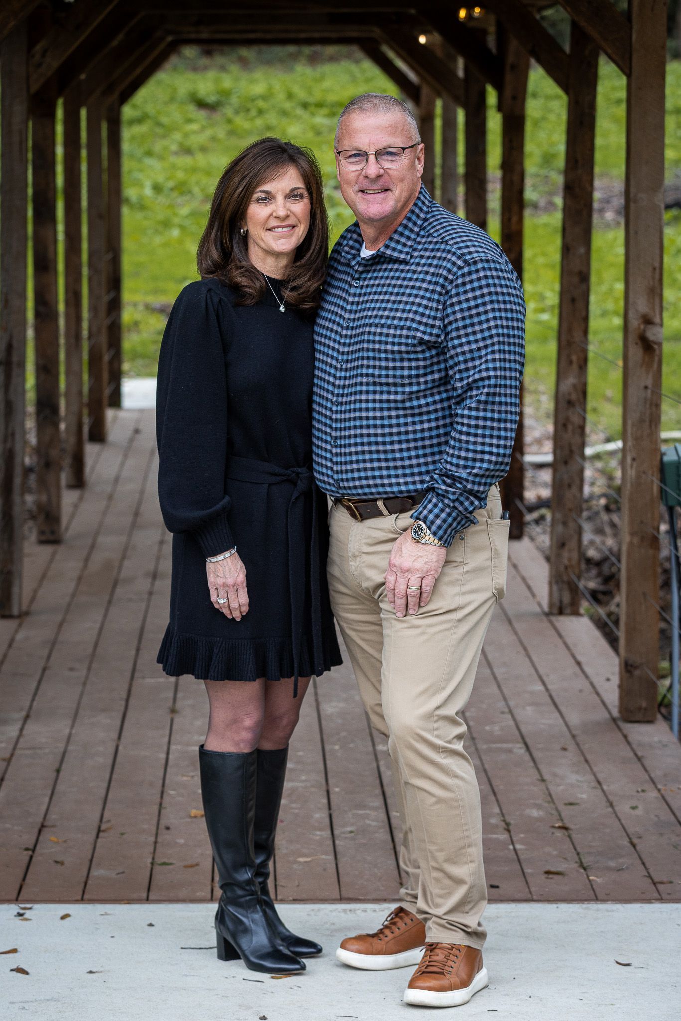 Couple standing, woman in black dress, man in blue striped shirt and khakis, on wooden walkway.