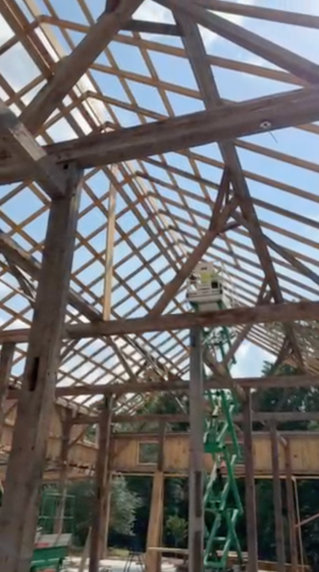 Wooden frame construction, interior view with a birdhouse and green lift platform visible. Sky in background.