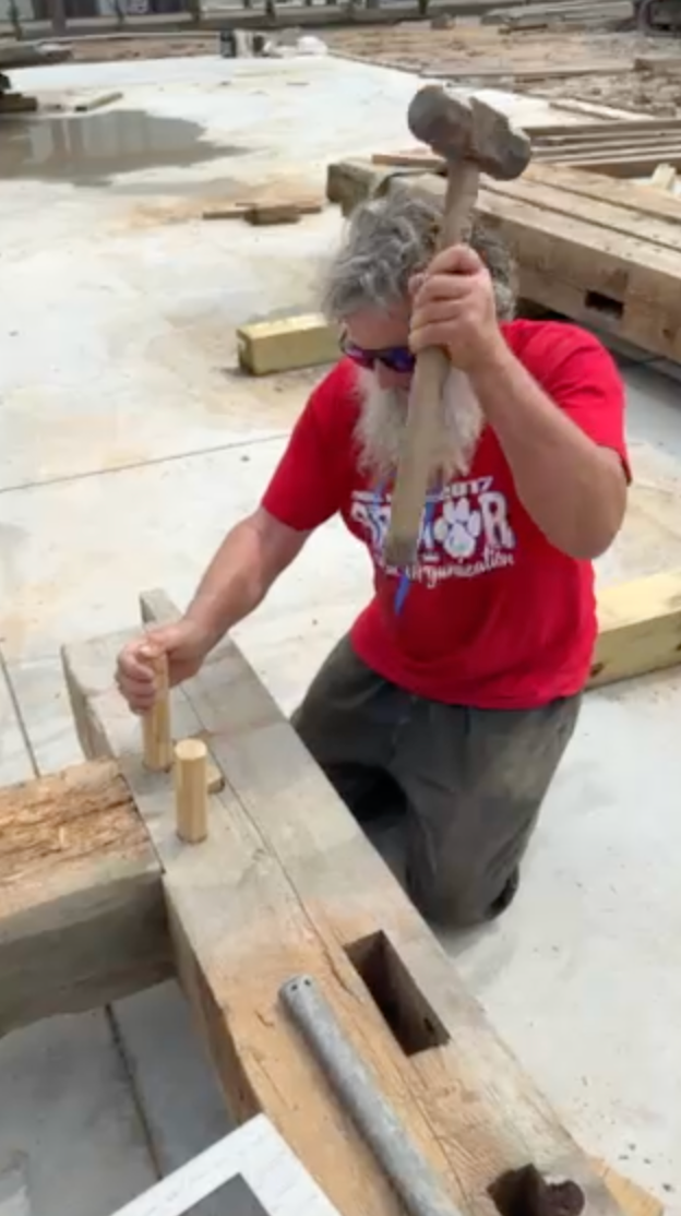 A person hammering a wooden peg into a beam on a concrete floor.