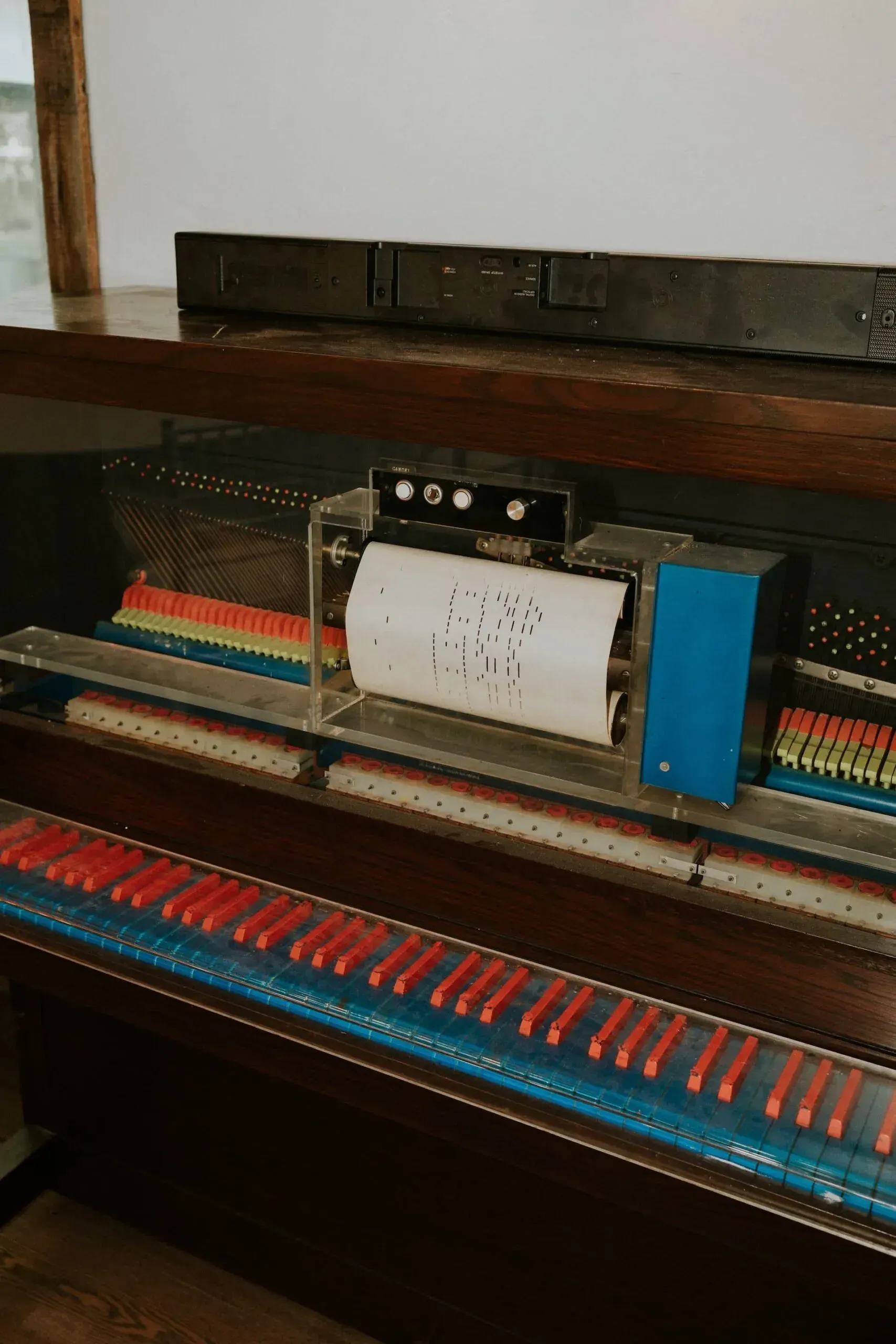 Piano with automated mechanism; paper roll with holes plays notes. Red/blue keys.