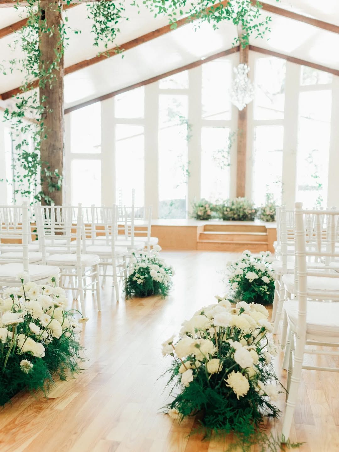 Wedding ceremony hall with white chairs, floral arrangements, and large windows.
