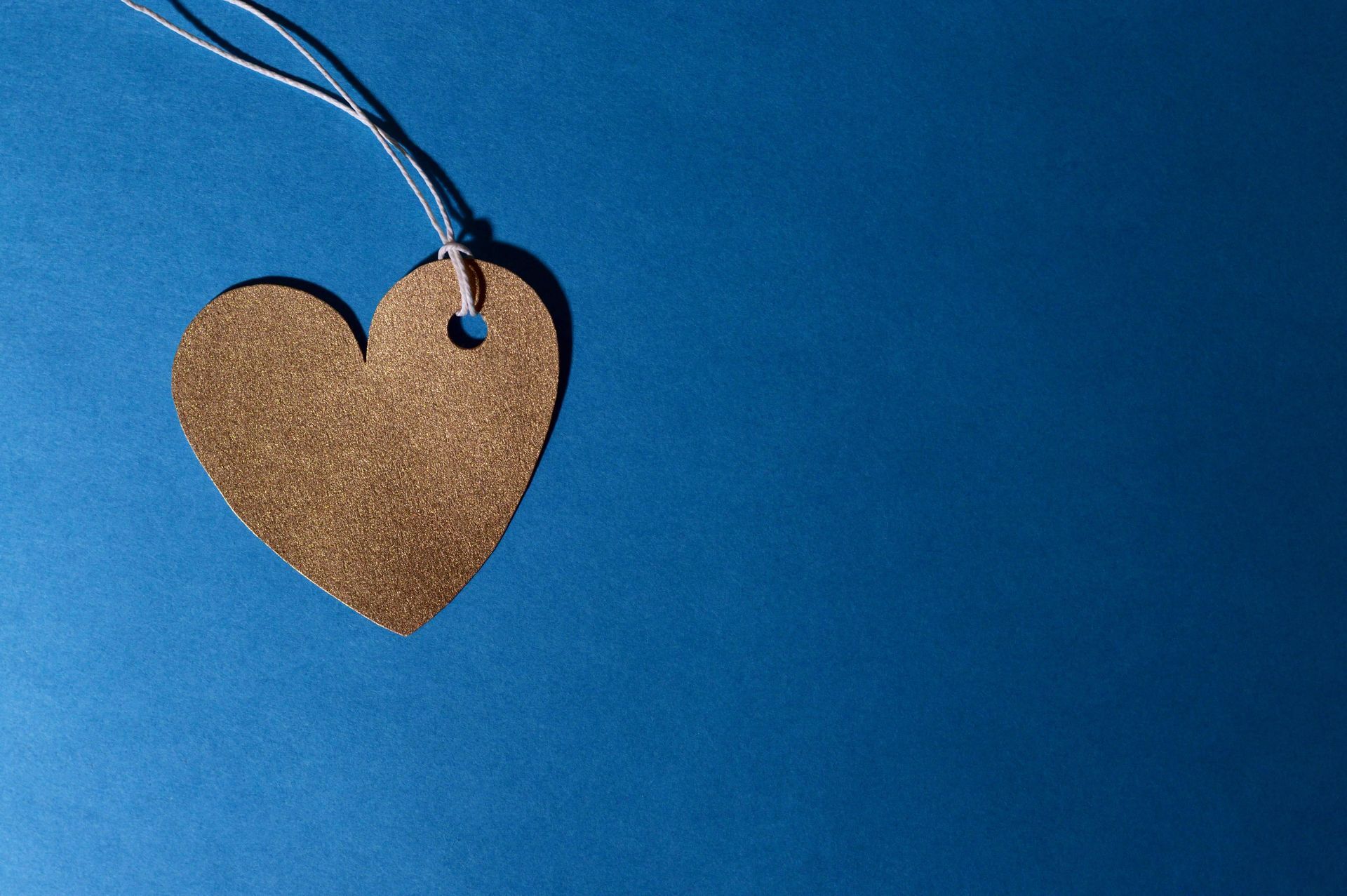 A golden coloured heart attached to a string placed on a blue background