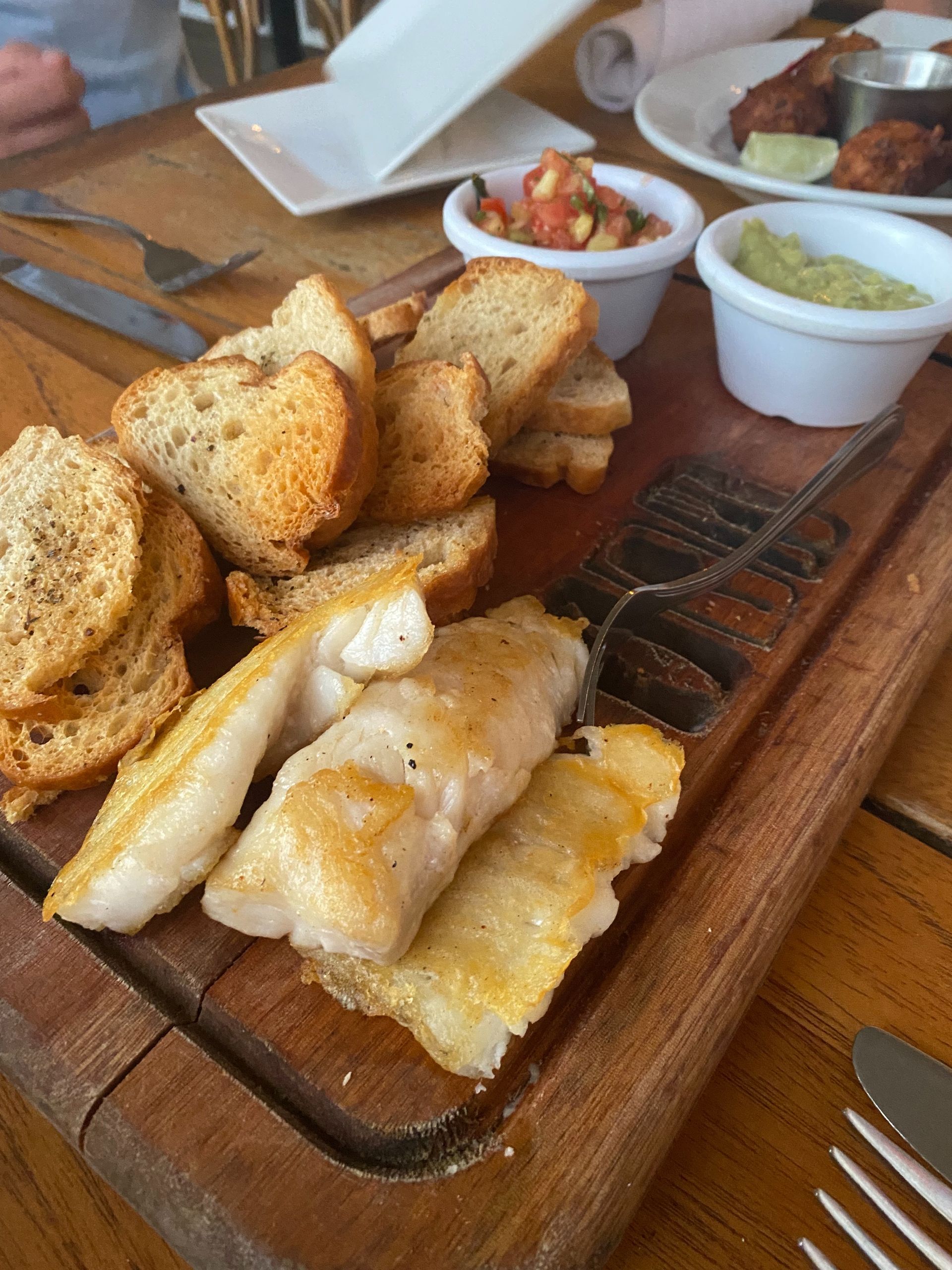 Toast with pan fried lion fish filets on a wooden cutting board with condiments  