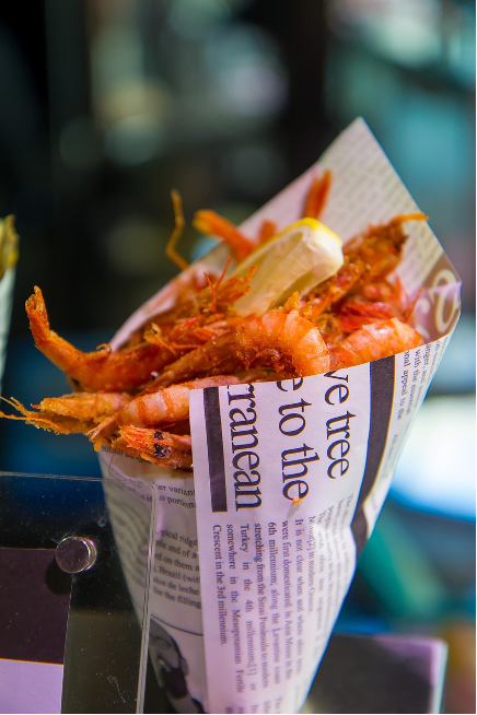 Fried shrimp in a paper cone with a lemon wedge.