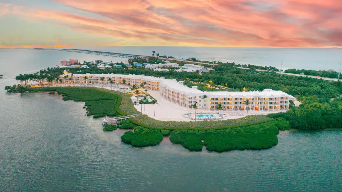Aerial view of  Isla Bella resort in Marathon, FL, with white buildings, green mangroves, and calm water at sunset