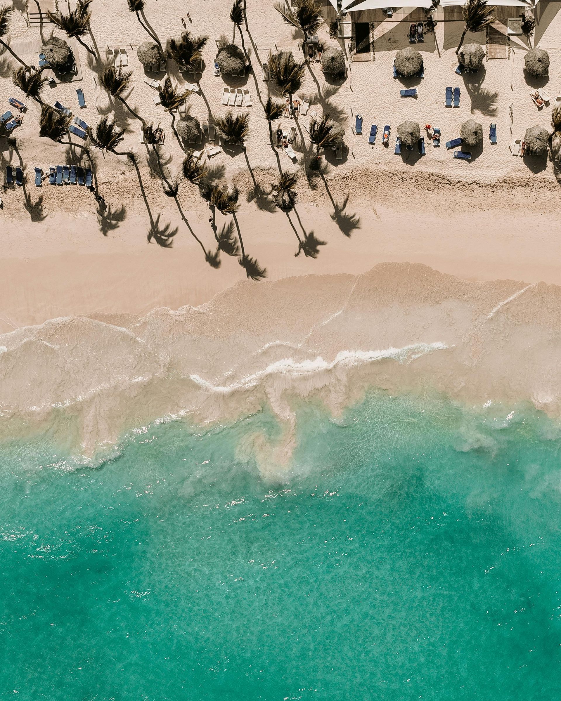 Aerial view of a beach with turquoise water, white sand, palm trees, and a resort area.