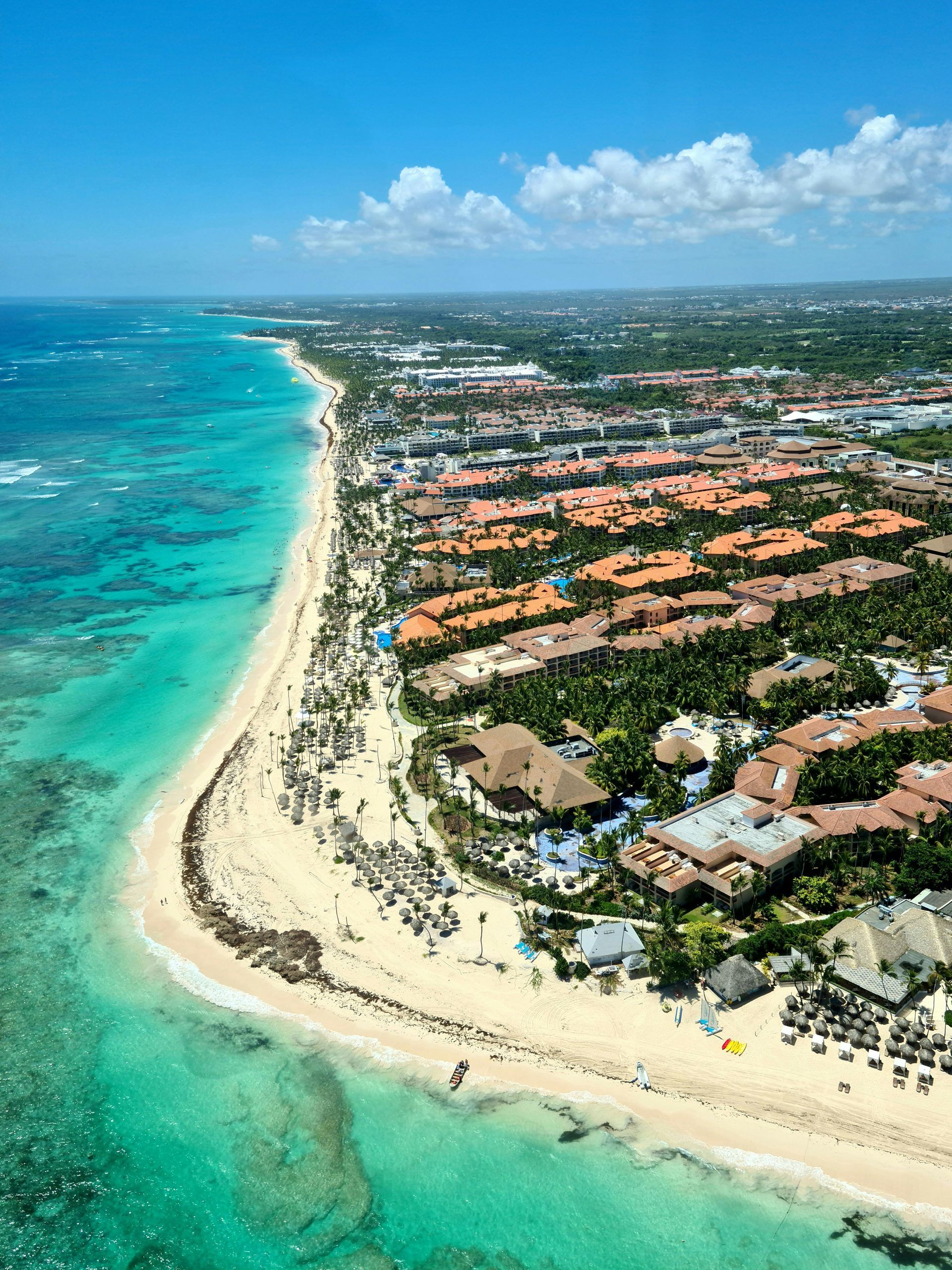 Aerial view of a tropical beach with turquoise water, white sand, and a coastal resort town in Punta Cana