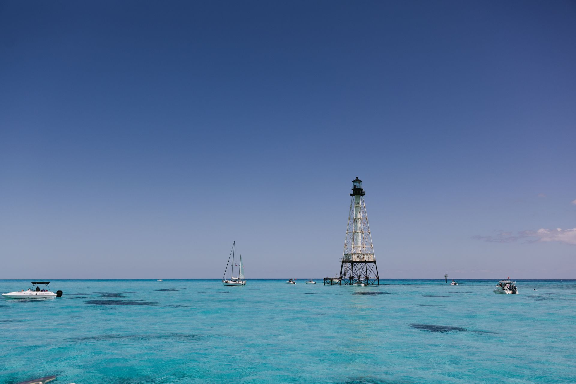 Turquoise sea in Florida Keys with small boats and a lighthouse on a distant offshore tower under a clear blue sky