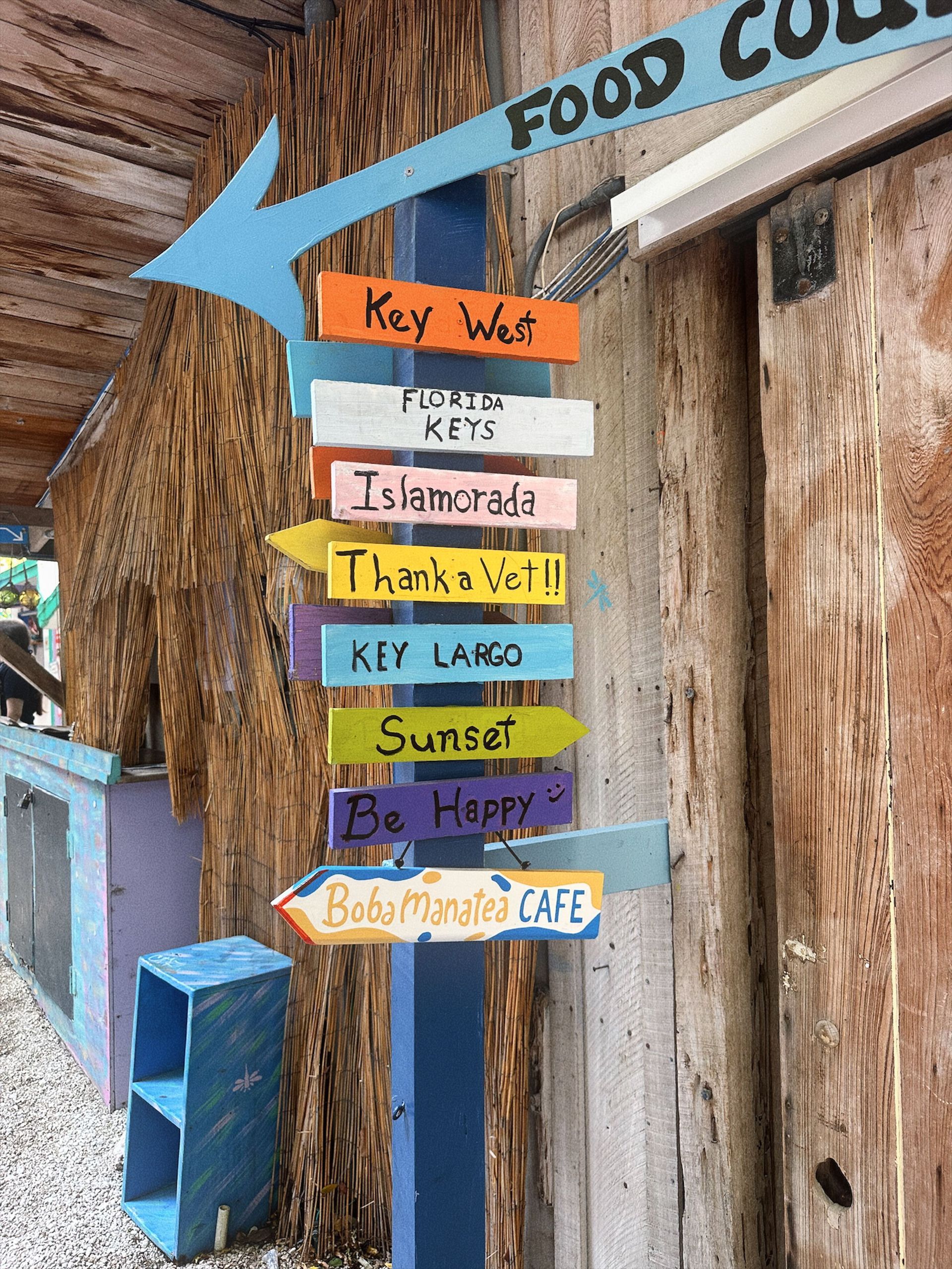 Colorful wooden directional signs with a large blue arrow mounted on a rustic post outdoors Florida keys