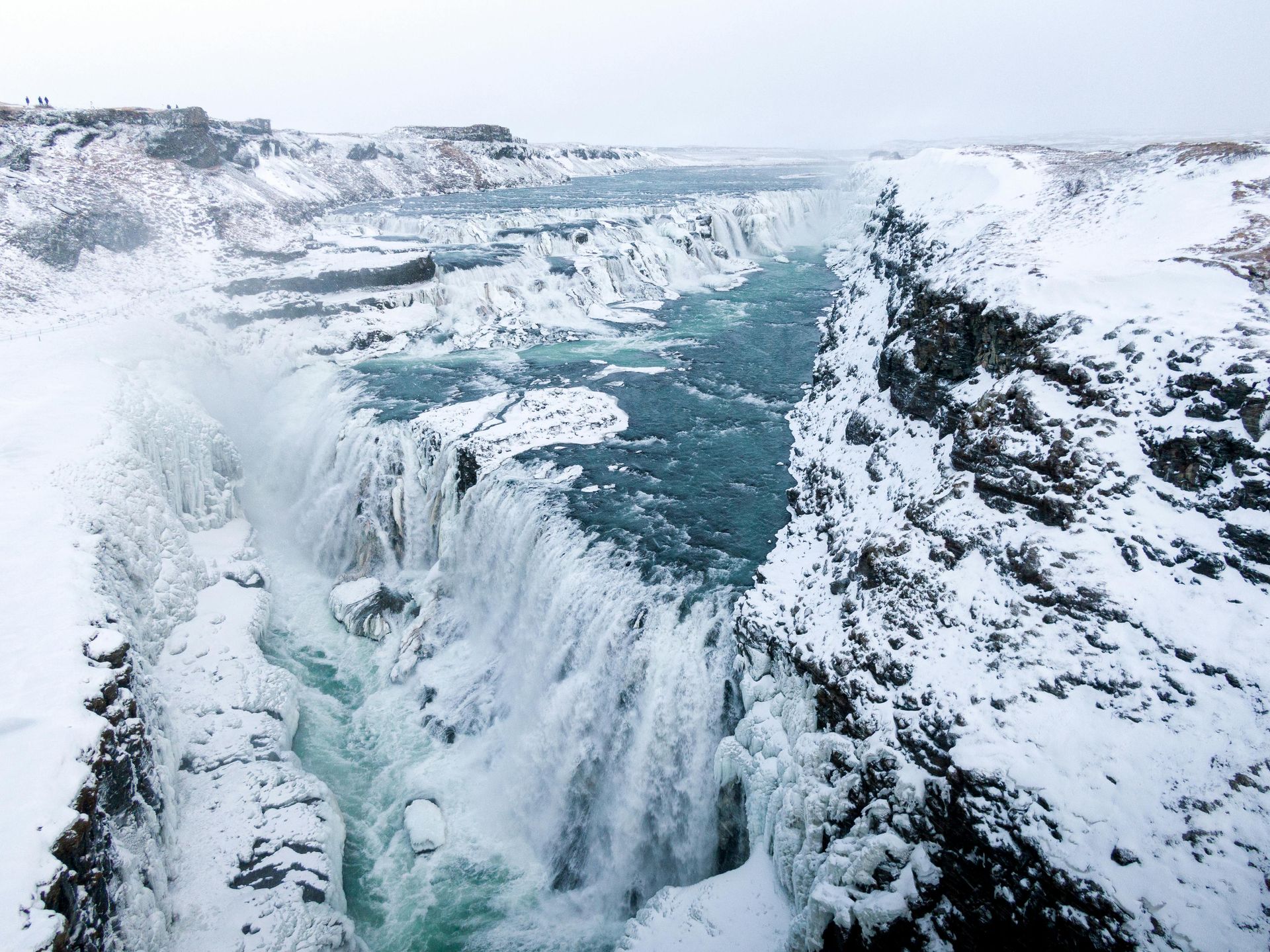 Gullfoss waterfall in Iceland during winter, with glacial blue water plunging through snowy, rugged rock canyons.
