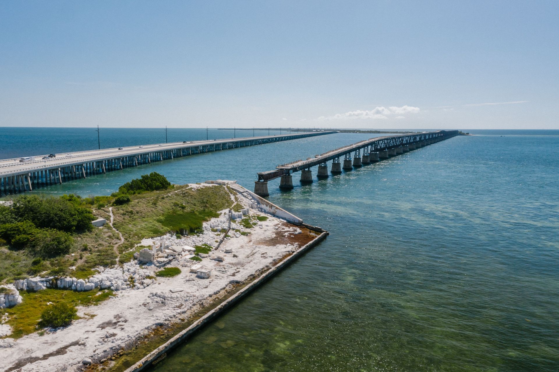 7 mile Long bridge over blue water  in Florida Keys beside a sandy, grassy shoreline under a clear sky