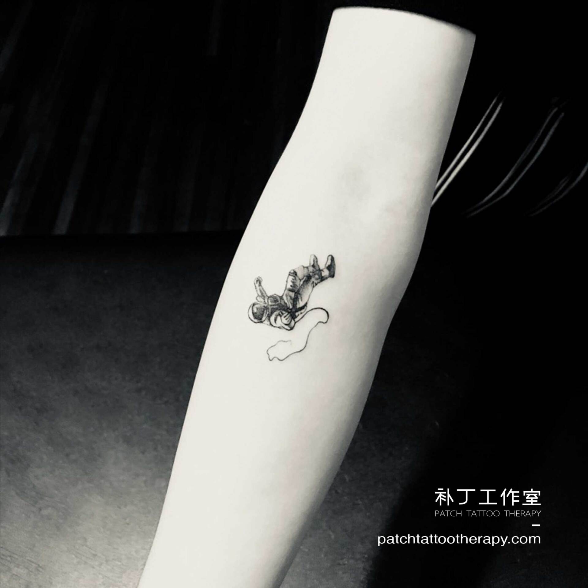 Inner forearm tattoo of a falling astronaut in micro mini style designed by Jingxi Gu at Patch Tattoo Therapy - angle 2