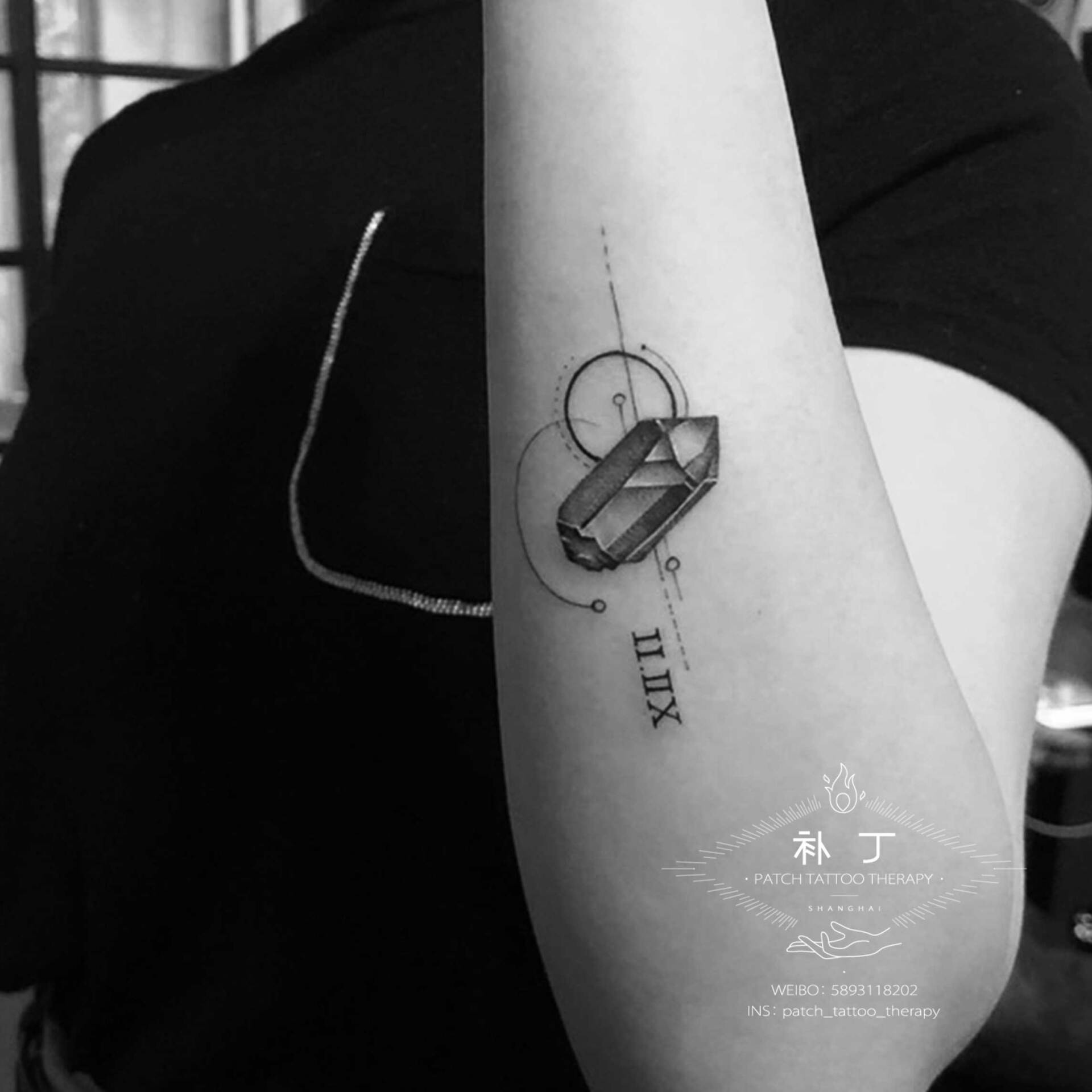 Forearm tattoo of a gem with roman letters in geometric style designed by Jingxi Gu at Patch Tattoo Therapy
