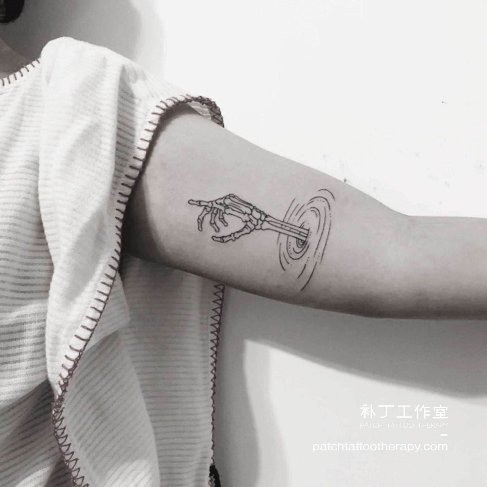 Inner arm tattoo of a pointing skeleton hand emerging from the water in outline form designed by Jingxi Gu at Patch Tattoo Therapy