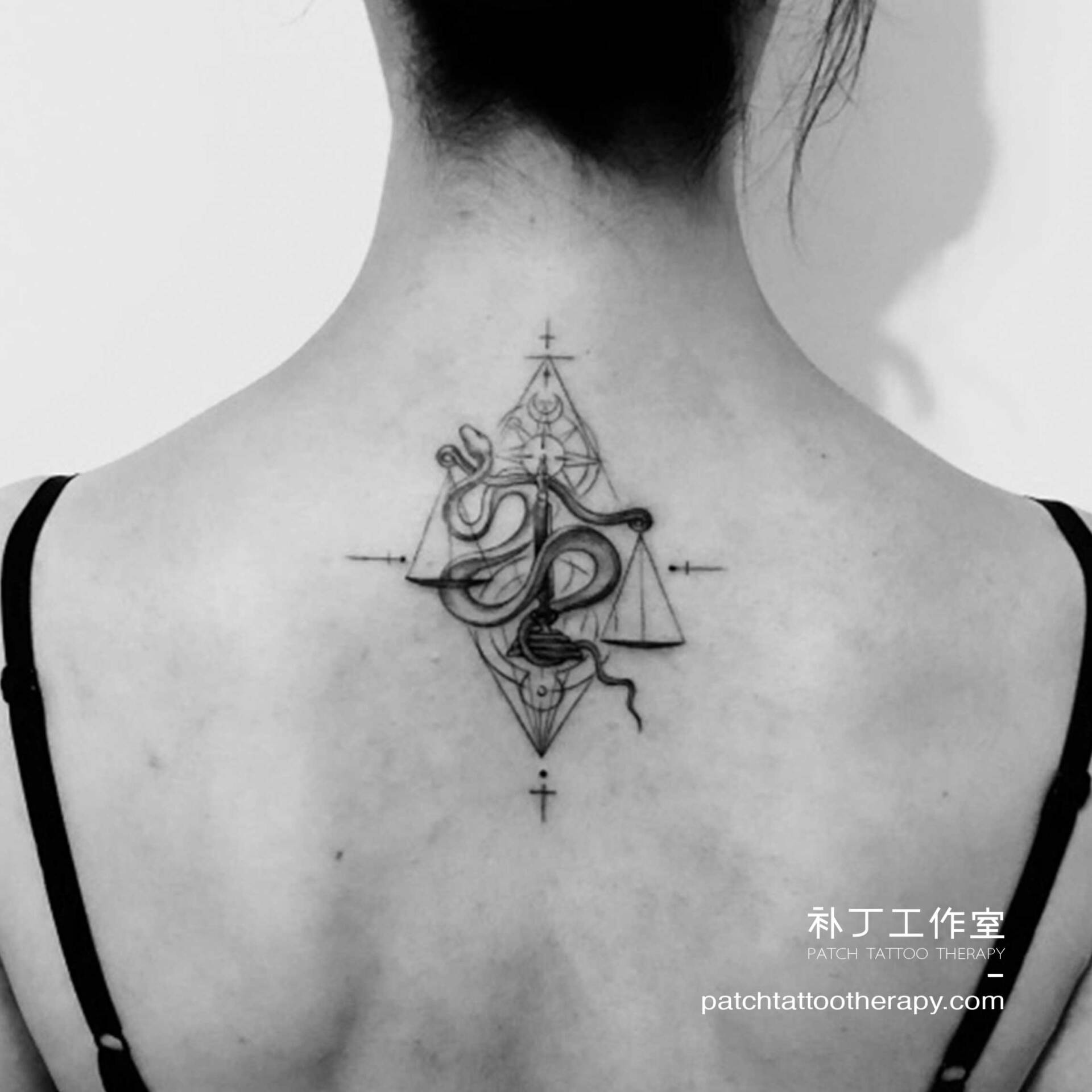 Back tattoo of a snake controlling a pair of traditional scales in geometric style designed by Jingxi Gu at Patch Tattoo Therapy