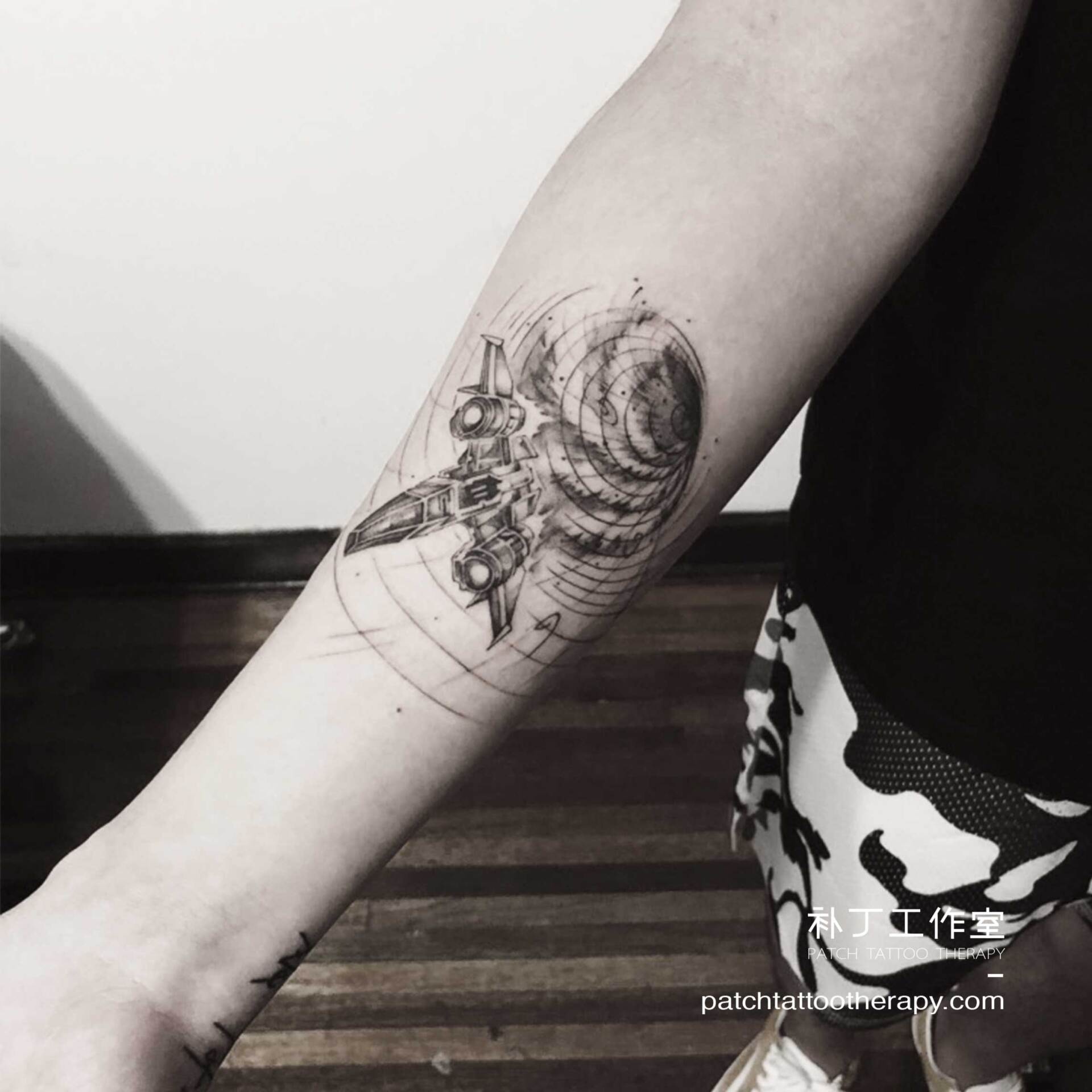 Inner forearm tattoo of a spaceship escaping a grid vortex hole in geometric style designed by Jingxi Gu at Patch Tattoo Therapy - angle 1