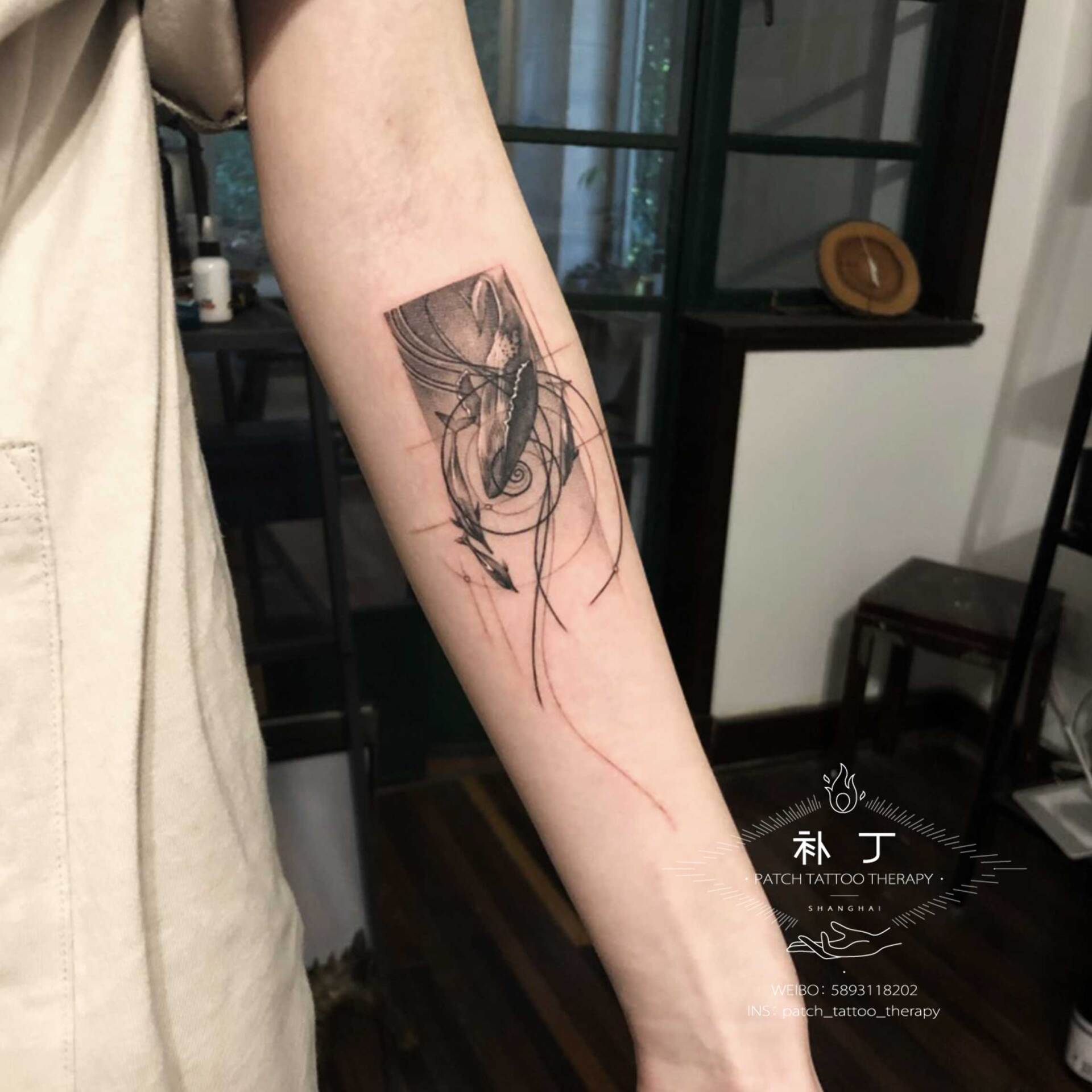 Inner forearm tattoo of a whale swimming with dolphins with a cochlea spiral shape background in geometric style designed by Jingxi Gu at Patch Tattoo Therapy - angle 2