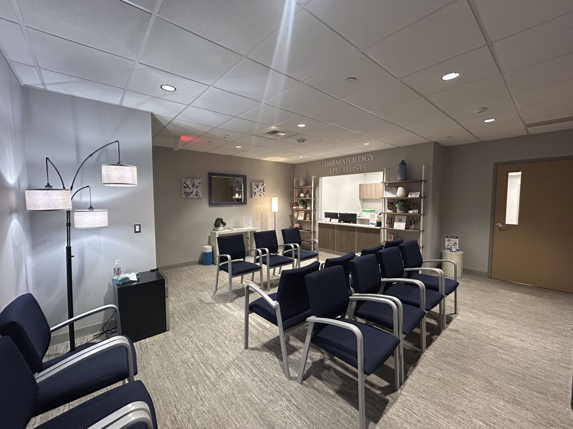 Waiting room with rows of blue chairs, neutral carpet, and a receptionist area in the background.