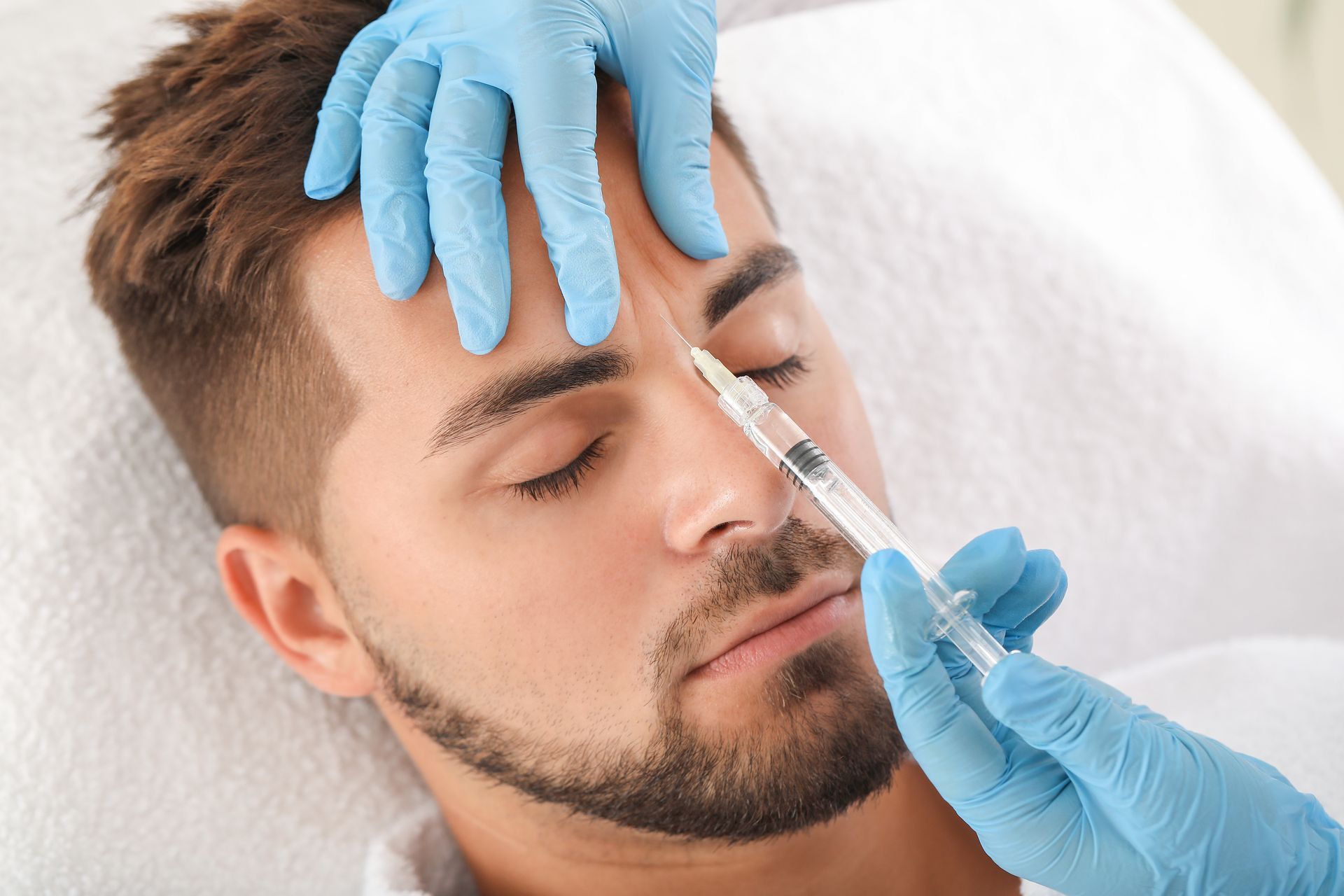 A man receiving a Botox injection in a clinic from an aesthetician. A man receiving a Botox injection in a clinic from an aesthetician.