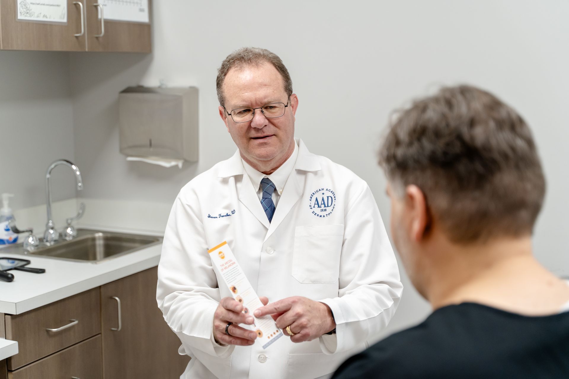 Doctor in a white coat talking to a patient; holding medication in a medical exam room.