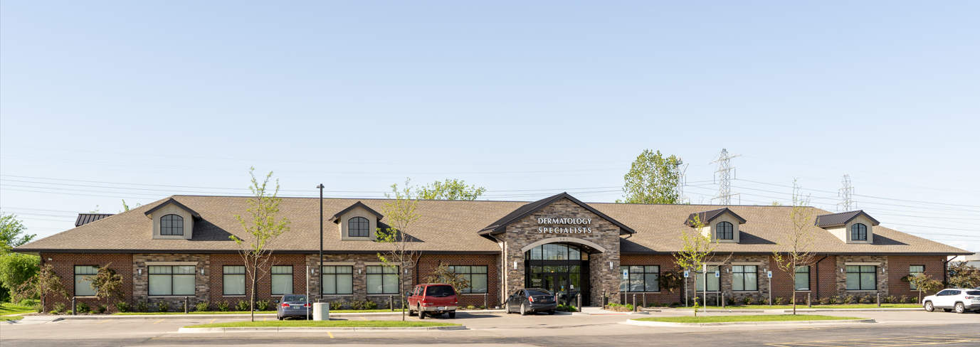A long, single-story brick building with a dark entryway under a stone arch.  Cars are parked nearby.