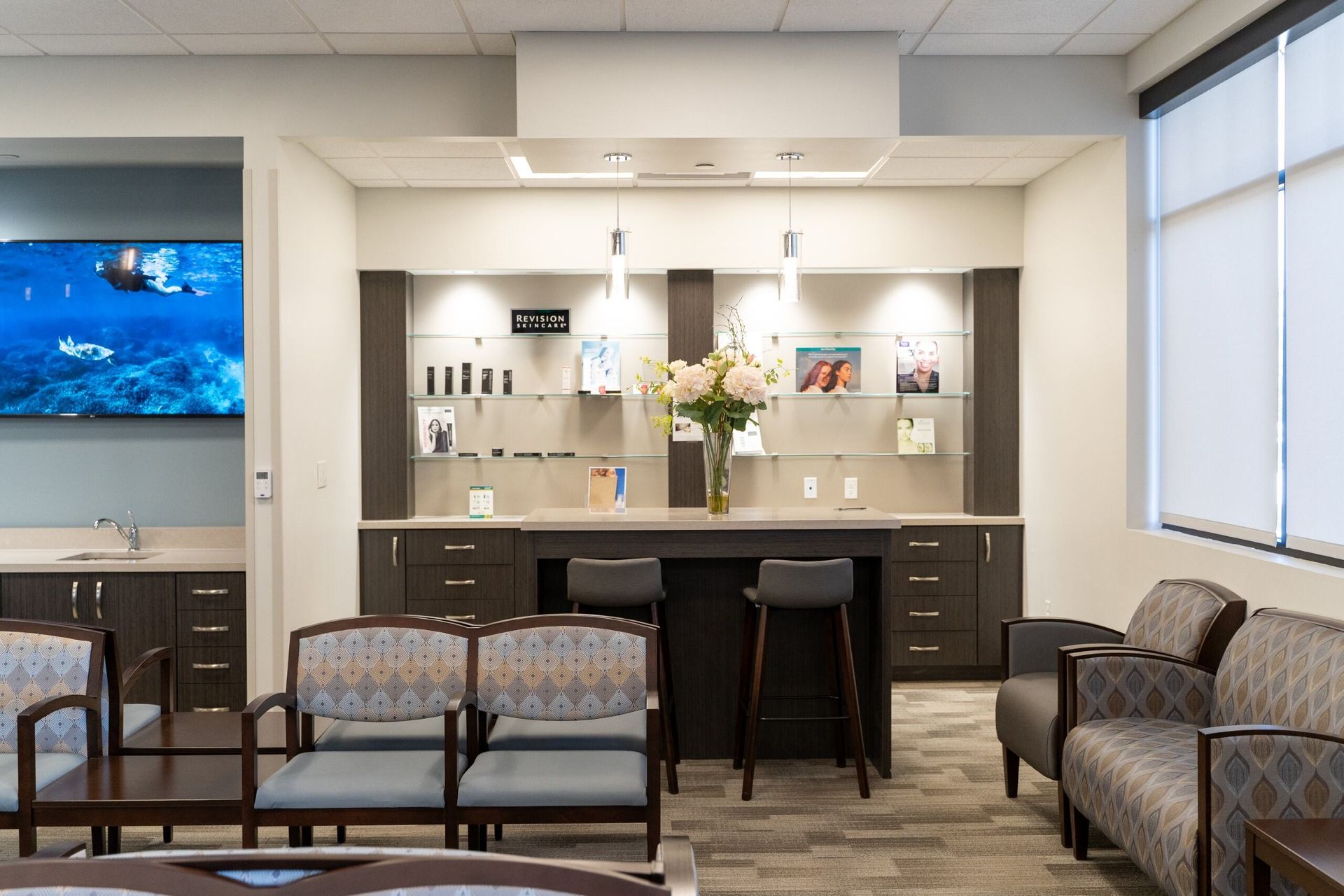 Modern waiting room with display shelves, seating, and TV screen showing underwater scene.