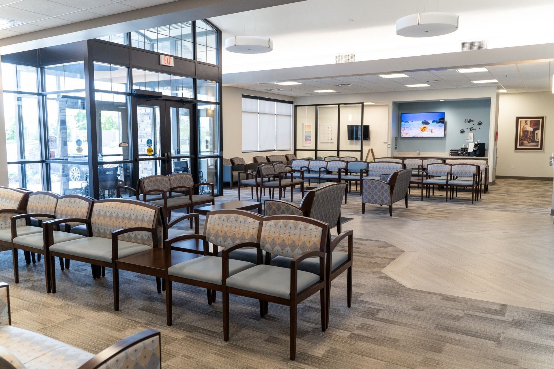 Waiting room with rows of chairs, glass doors, and a television on the wall.