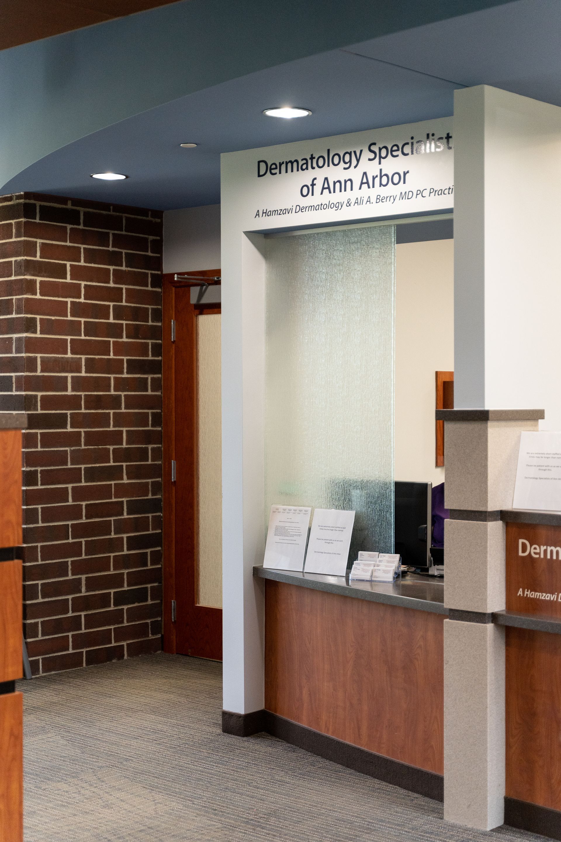 Reception area: Dermatology Specialists of Ann Arbor. Brick wall, front desk, frosted glass, wood accents.