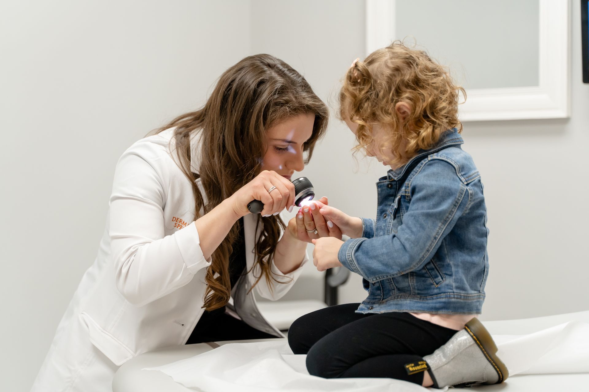 Doctor examining a child's finger with a dermatoscope in a clinic setting.