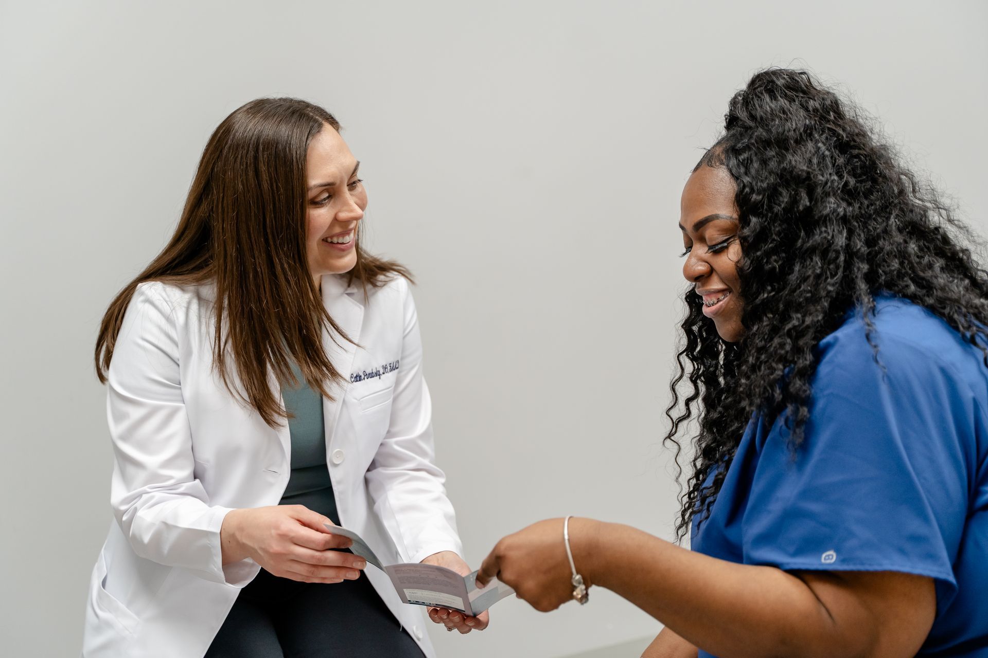 Doctor in white coat showing cards to smiling woman in blue scrubs.