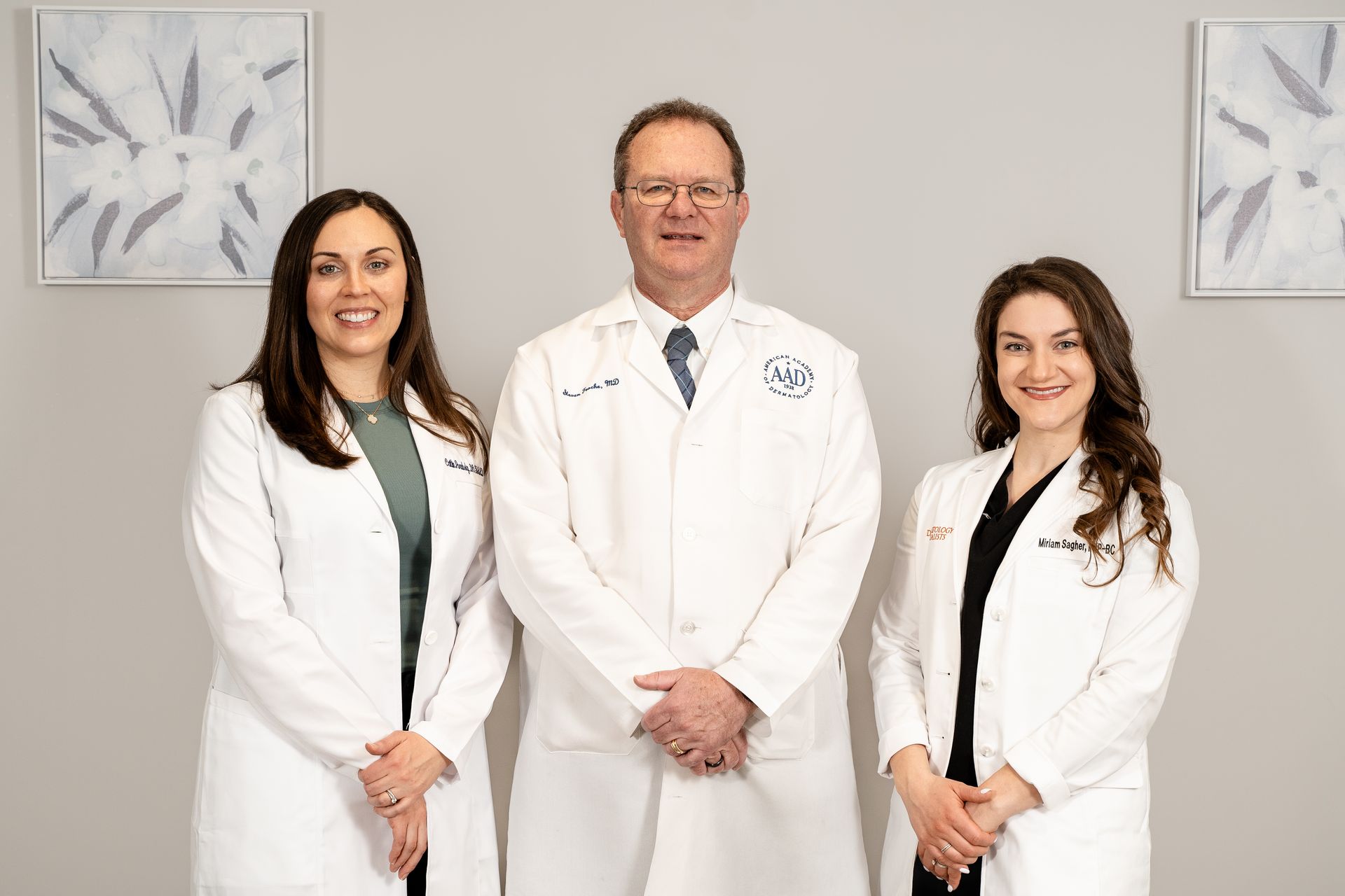 Three medical professionals in white coats stand in a room with artwork.