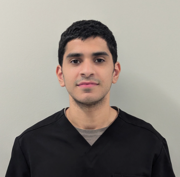 Man in black scrub top against a gray background, looking forward.