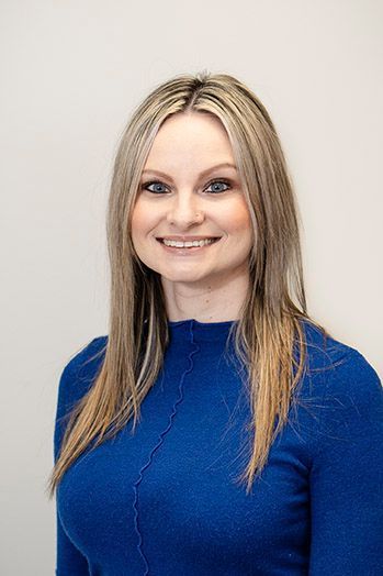 Woman with blonde hair smiles, wearing a blue sweater, against a white background.
