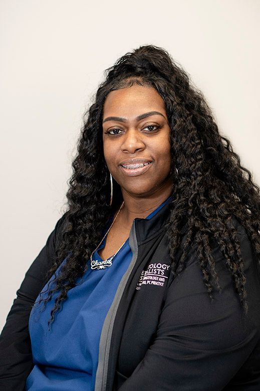 Woman with dark curly hair and braces, wearing a blue shirt and black jacket, smiles at the camera.