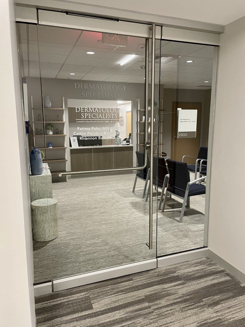 Glass doors leading into a waiting room, displaying a medical office with chairs and reception desk.