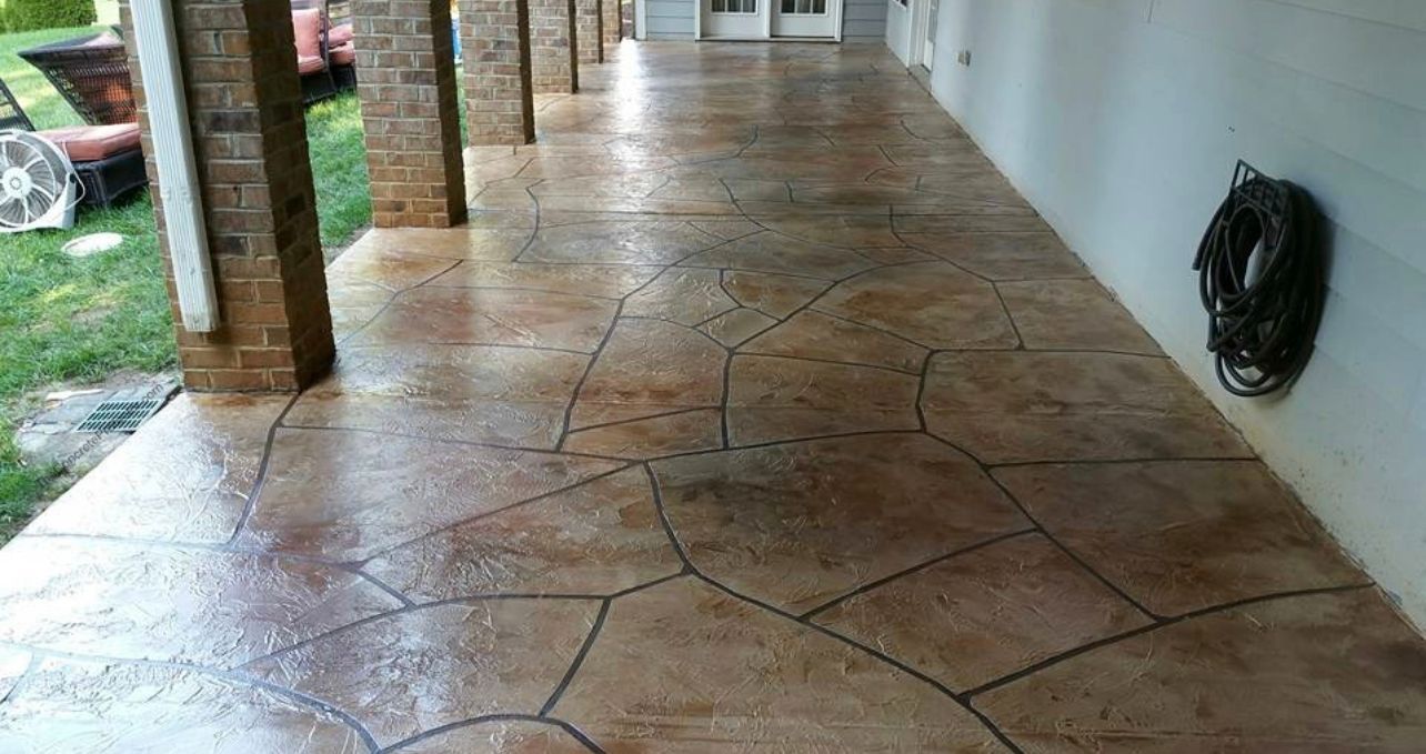 Stamped concrete porch, brown and tan, with a stone-like pattern. Columns and a water hose are visible.