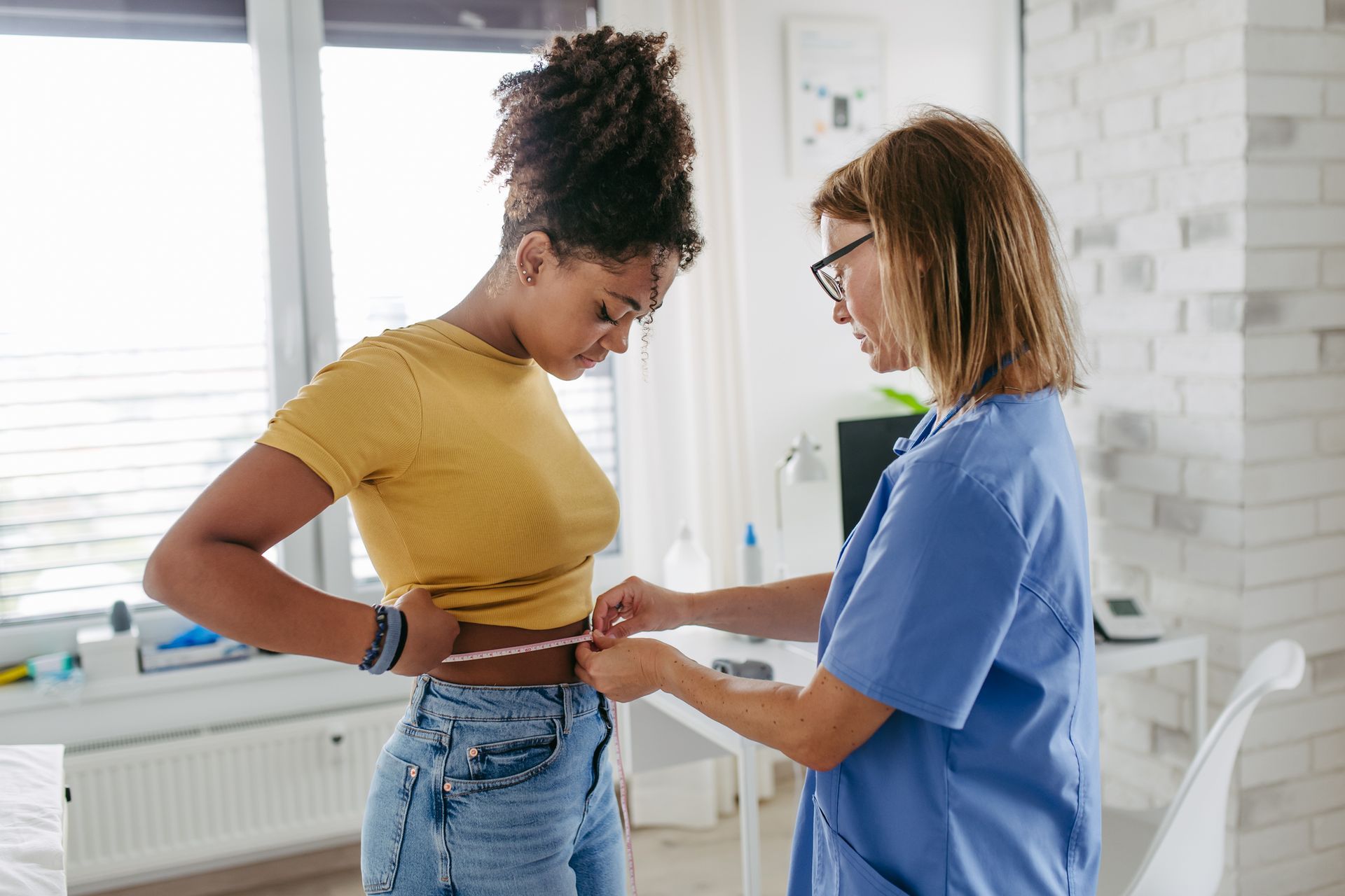 A person in a yellow shirt has their waist measured by a person in blue scrubs.