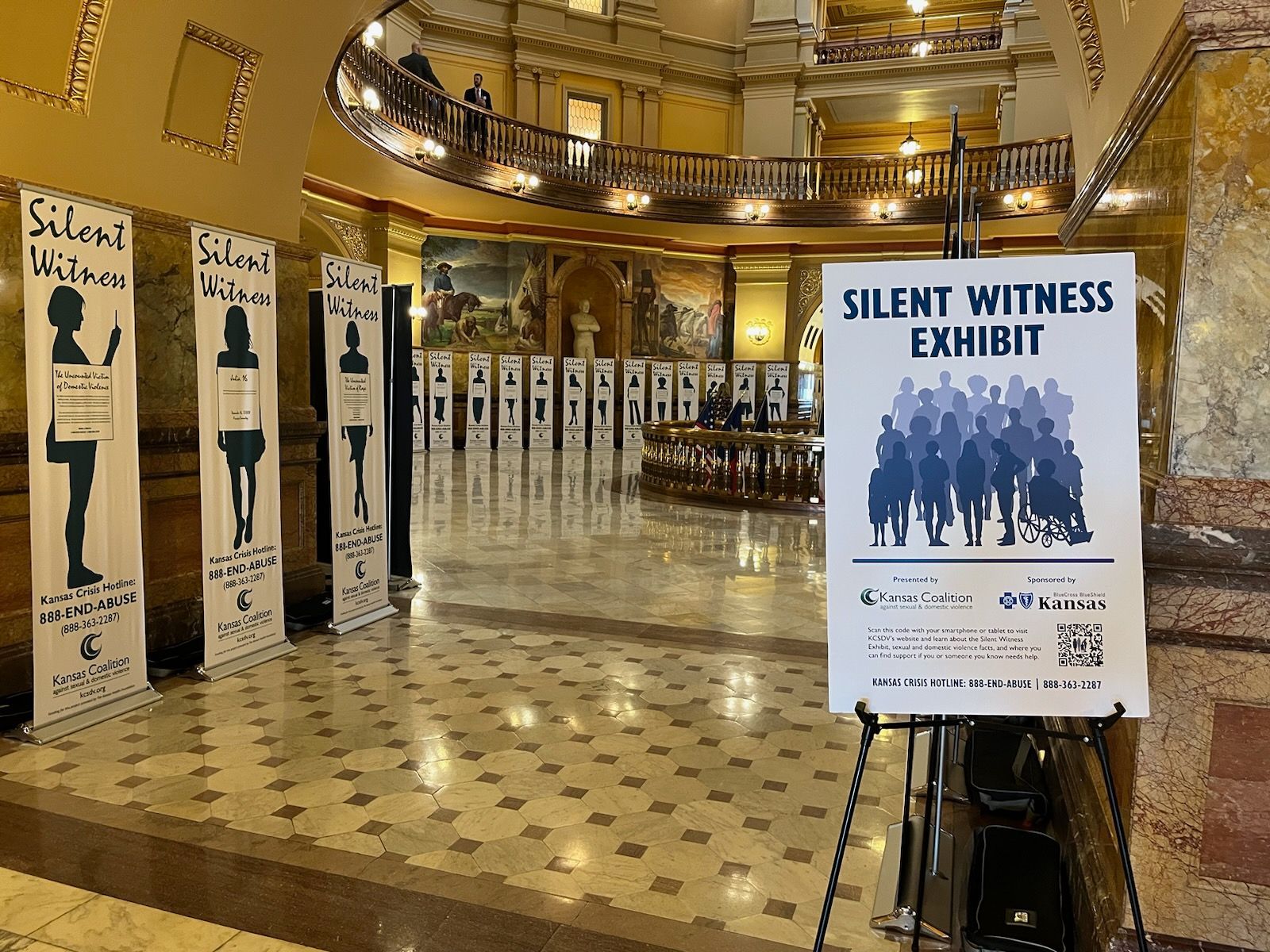 Silent Witness Exhibit in a building lobby: figures on display, signage and portraits.