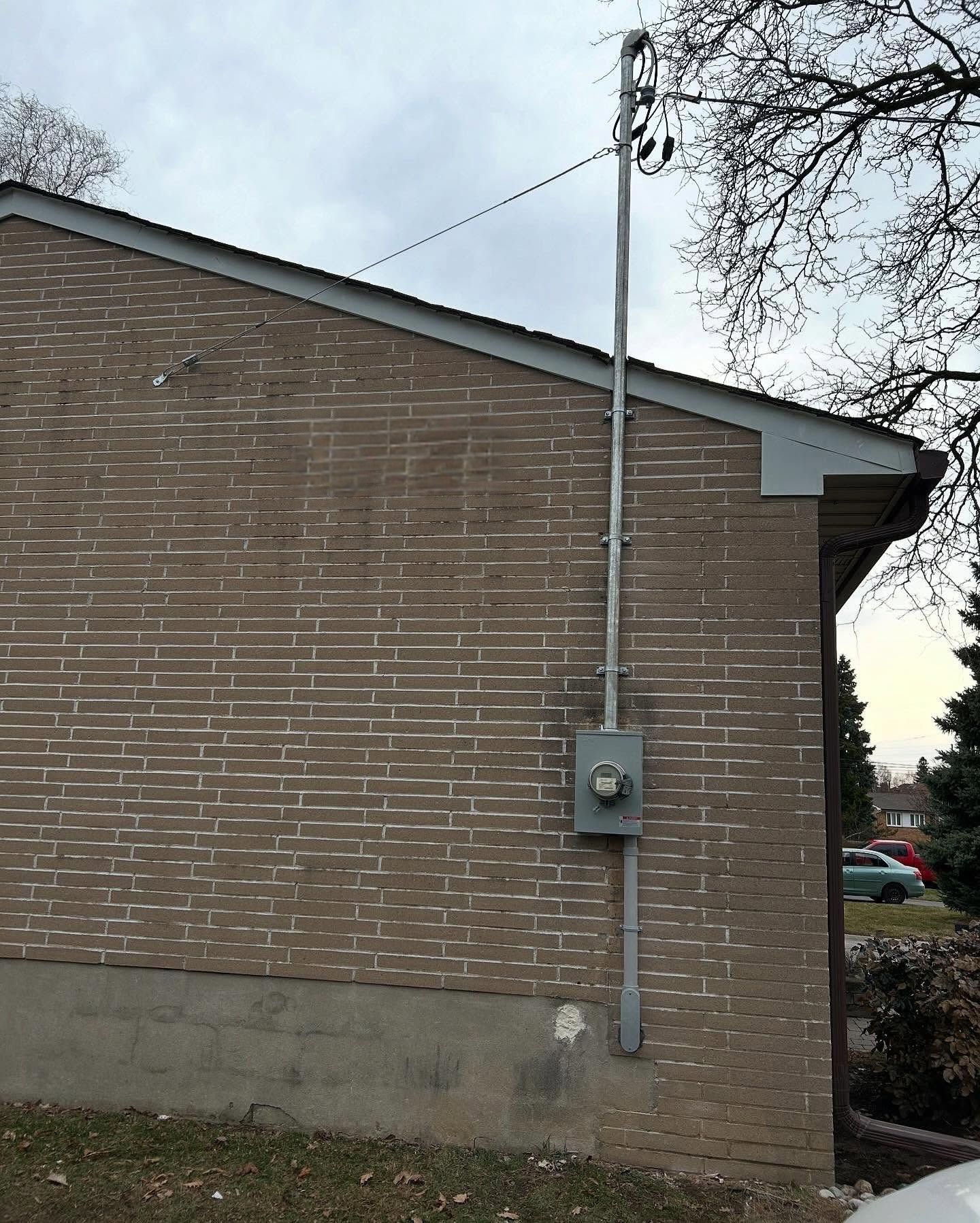 Brick building wall with electrical meter and conduit mounted beside a window under a gray sky