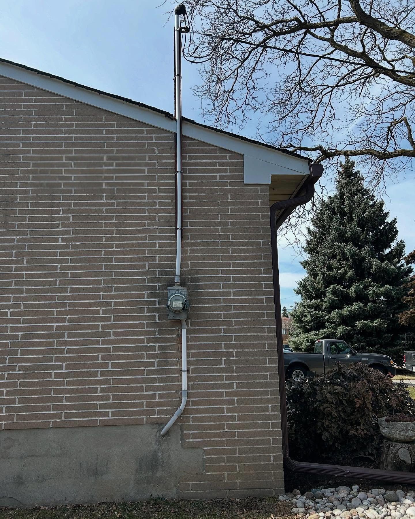 Brick house side wall with a utility meter and vertical conduit under a blue sky