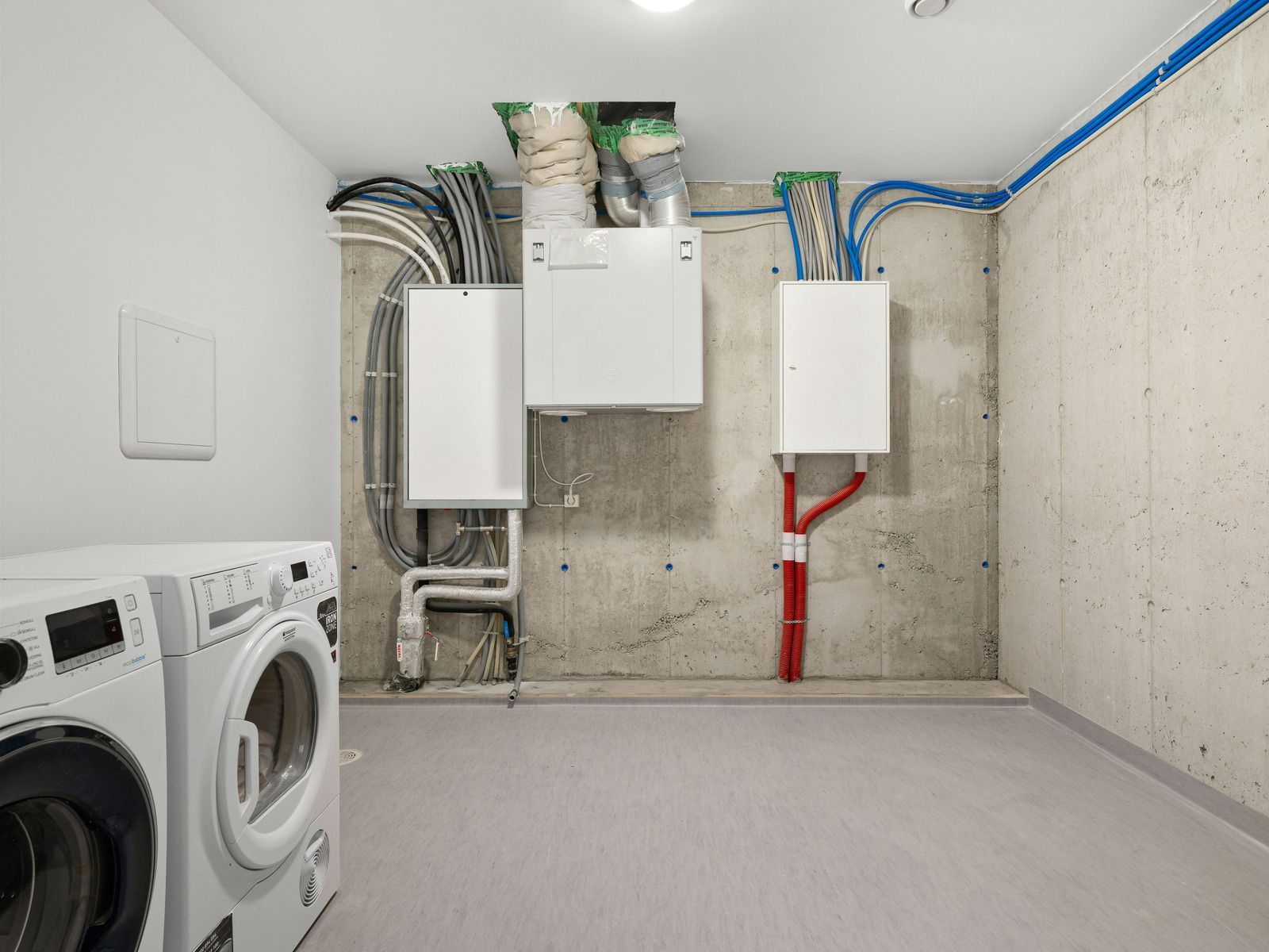 Two electricians in orange safety gear inspecting wiring in a small utility room and bathroom area.