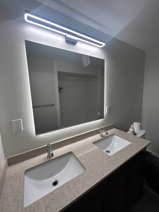Bathroom vanity with two sinks and a large backlit mirror above a speckled countertop.