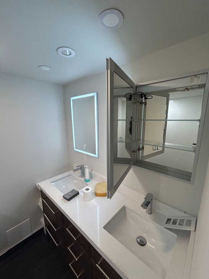 Modern bathroom vanity with double sinks, mirror cabinet, and white countertop under bright lighting
