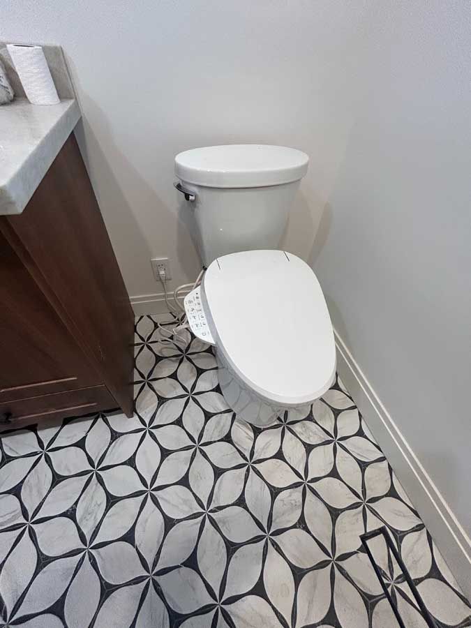 Small bathroom with a white toilet, patterned black-and-white floor tiles, and a vanity cabinet.