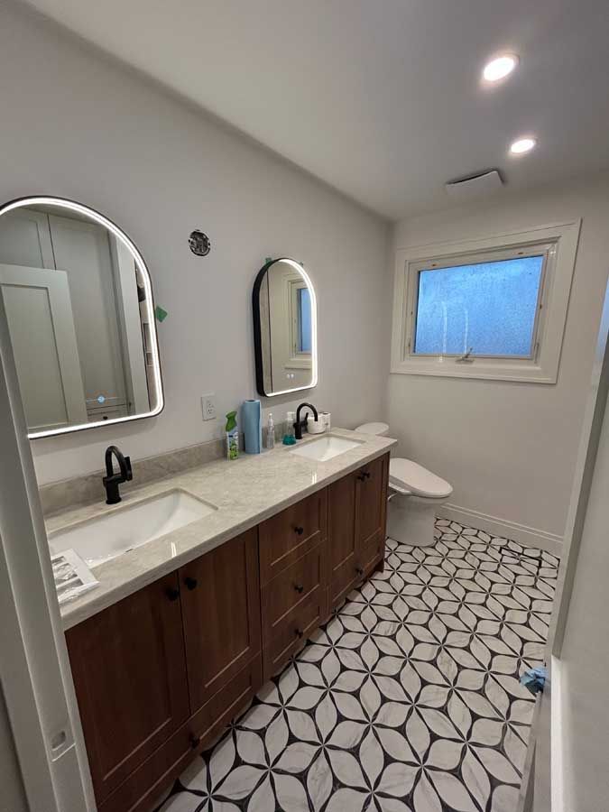 Modern bathroom with double vanity, arched mirrors, and patterned tile floor