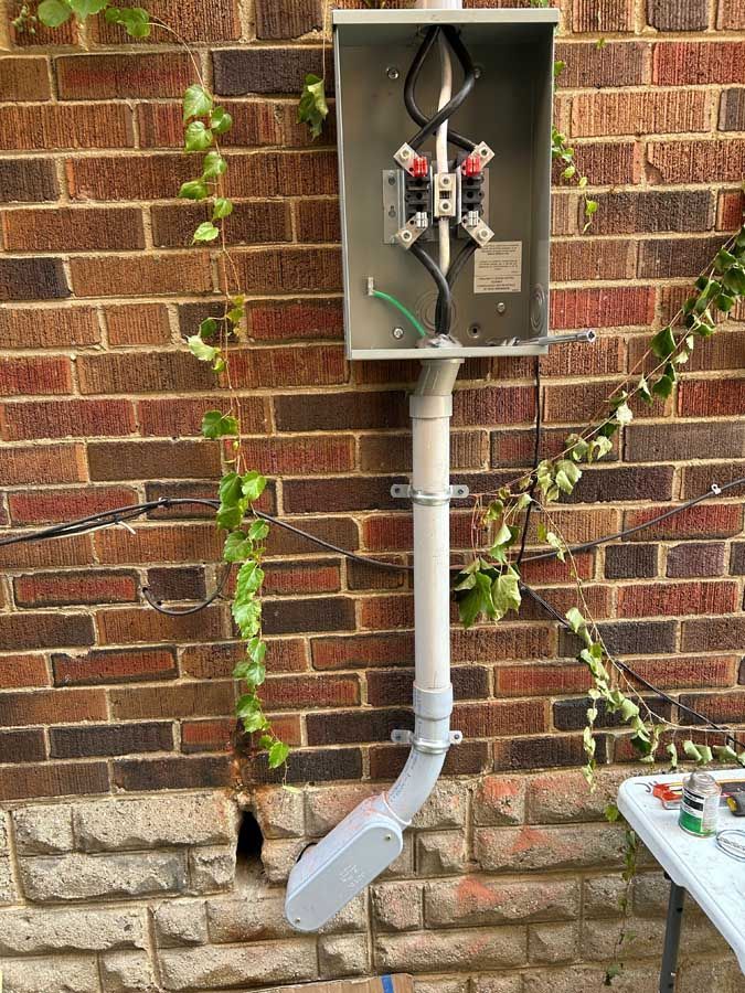 Electrical meter and conduit box mounted on a brick wall, with white PVC piping below.